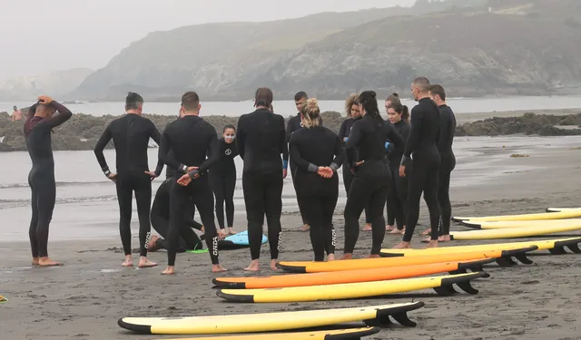 Grupo de alumnos en una clase de surf en grupo en la playa de Frexulfe