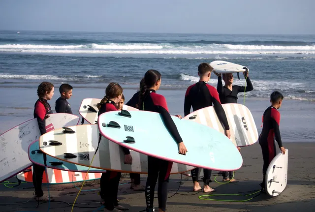 Alumnos con tablas de surf listos para su bono de clases en la playa de Frexulfe